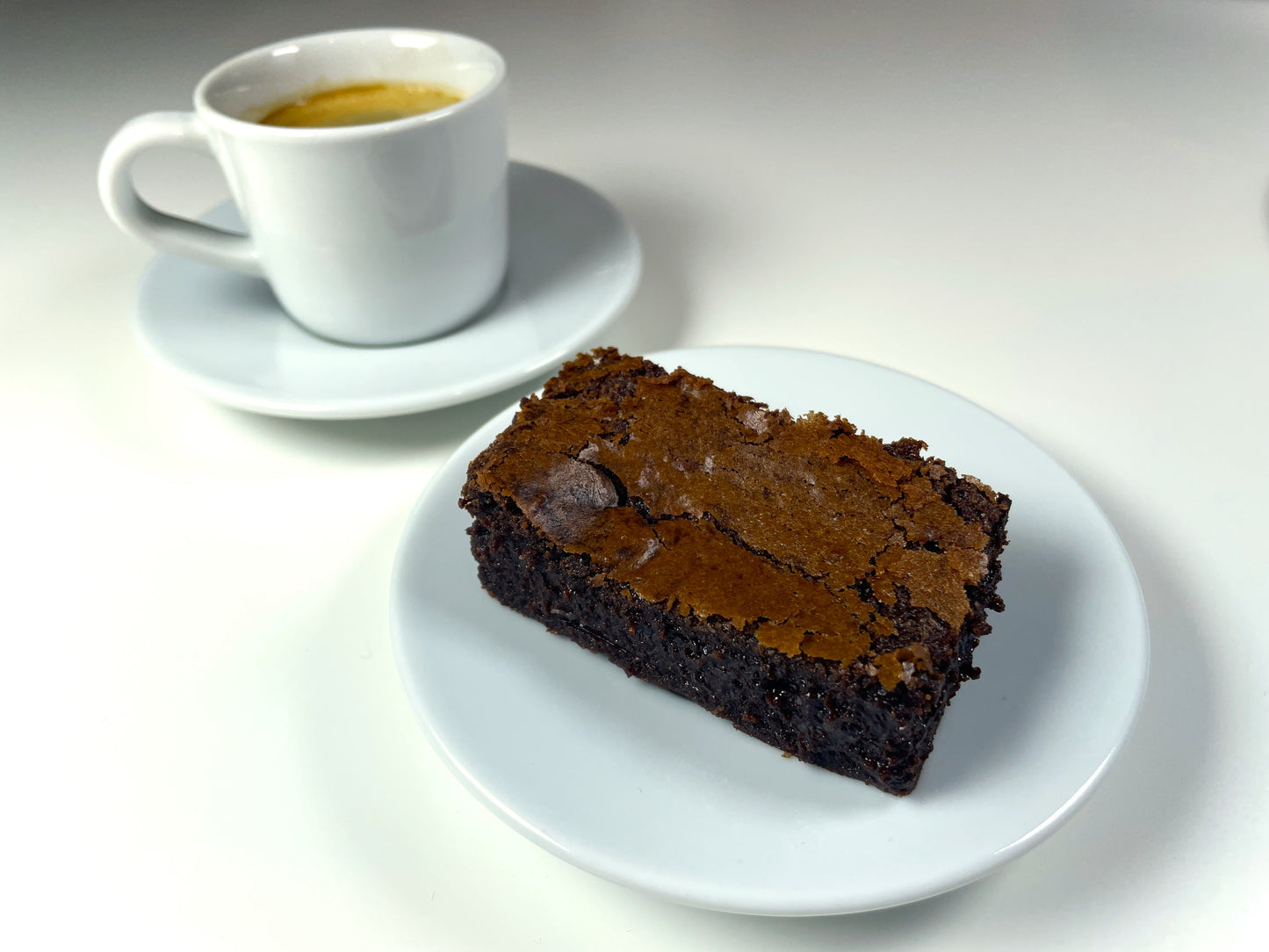 Rich, gooey brownie plated next to an espresso, a classic duo for chocolate and coffee lovers